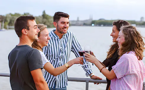 Group enjoying wine on Bateaux Bordelais Cruise with Bordeaux skyline in background.