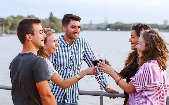 Group enjoying wine on Bateaux Bordelais Cruise with Bordeaux skyline in background.