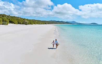 Walking along Whitehaven Beach, Whitsundays Island, with clear blue water and lush greenery.