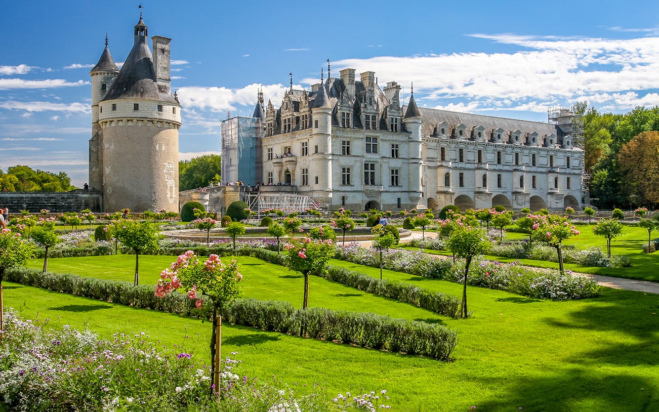 Chenonceau Castle with gardens in Loire Valley, featuring manicured lawns and blooming flowers.