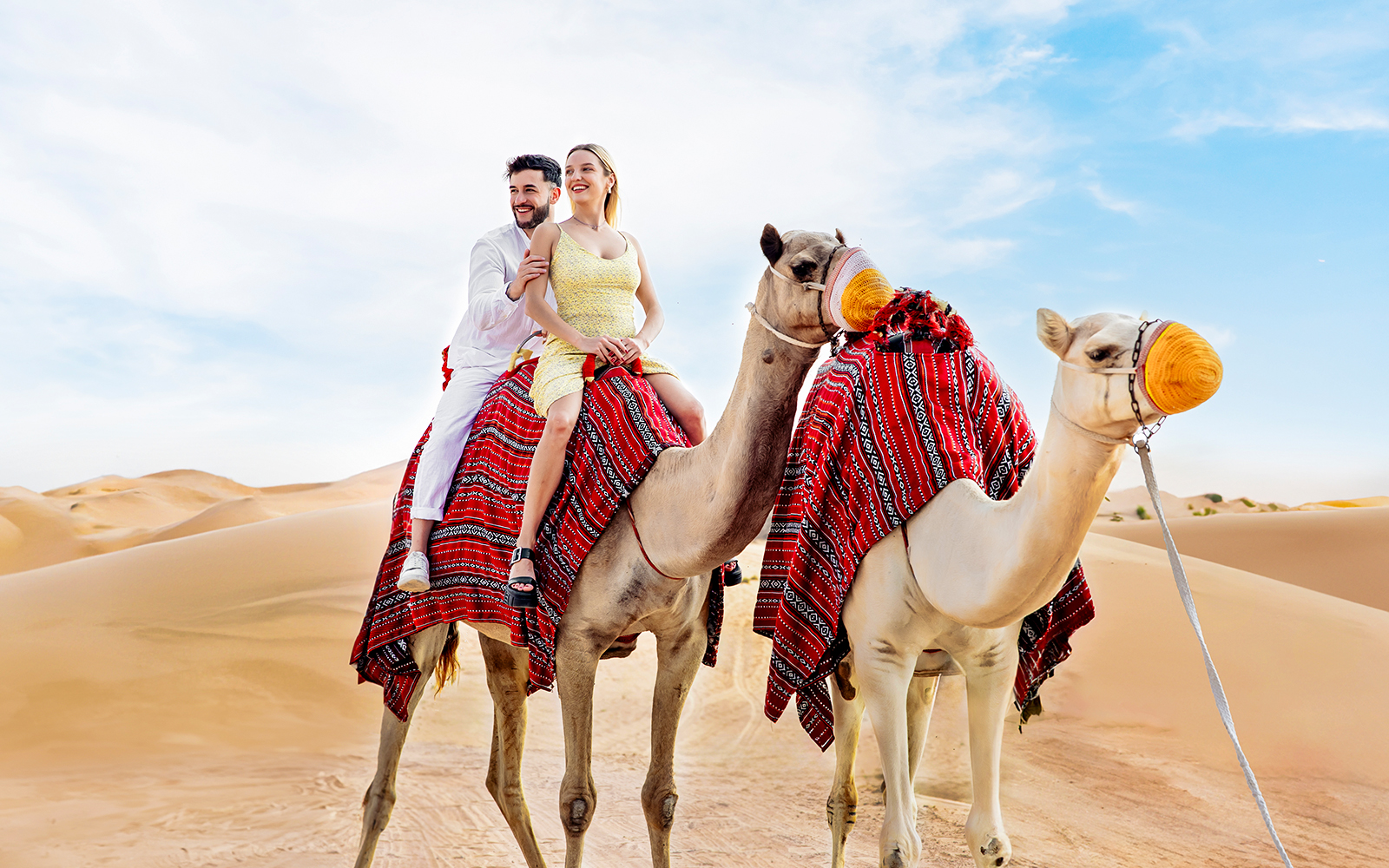 Couple riding camels in desert, part of Hot Air Balloon Experience with Vintage Land Rover Drive.