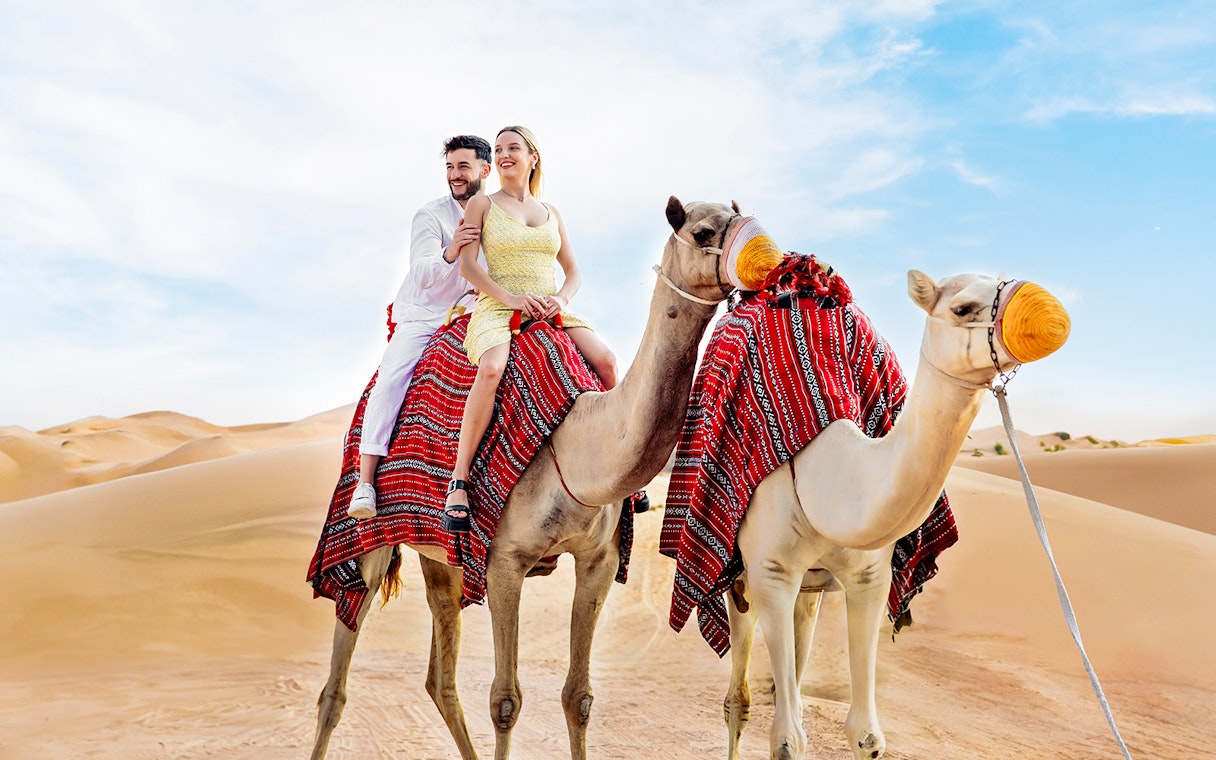 Couple riding camels in desert, part of Hot Air Balloon Experience with Vintage Land Rover Drive.