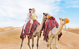 Couple riding camels in desert, part of Hot Air Balloon Experience with Vintage Land Rover Drive.