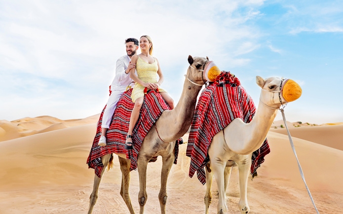 Couple riding camels in desert, part of Hot Air Balloon Experience with Vintage Land Rover Drive.
