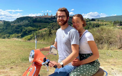 Couple on Vespa with San Gimignano skyline during Chianti sunset tour.