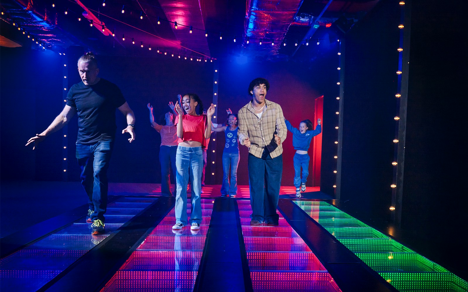 Participants on a lit glass bridge at Squid Games experience in London.