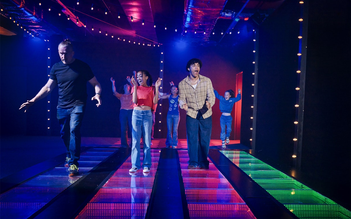 Participants on a lit glass bridge at Squid Games experience in London.