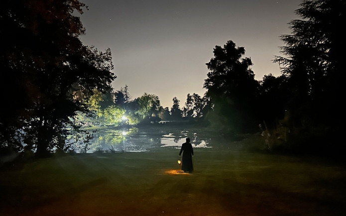 Silhouette of a person with a lantern by a lake at Viña Concha y Toro nighttime dinner show.