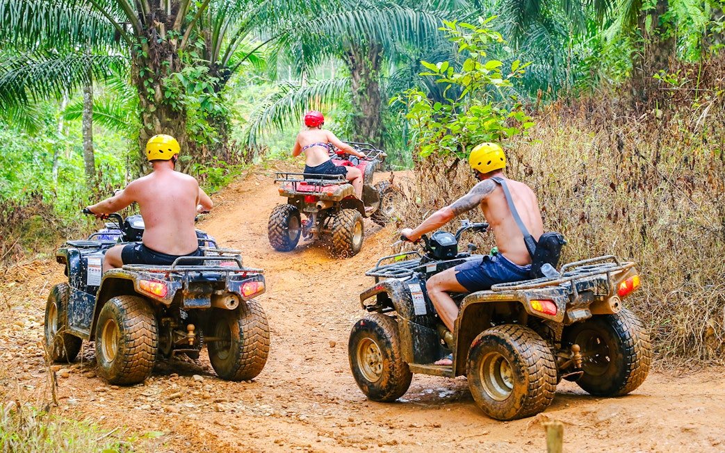 ATV riders navigating a dirt trail in Phuket's lush jungle.