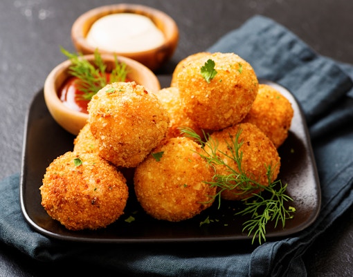 Croquettes served on a wooden board with dipping sauce in a restaurant setting.
