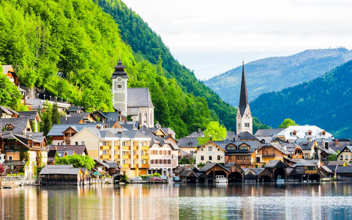 Wooden houses and church by the lake in Hallstatt, Austria, with lush green mountains.