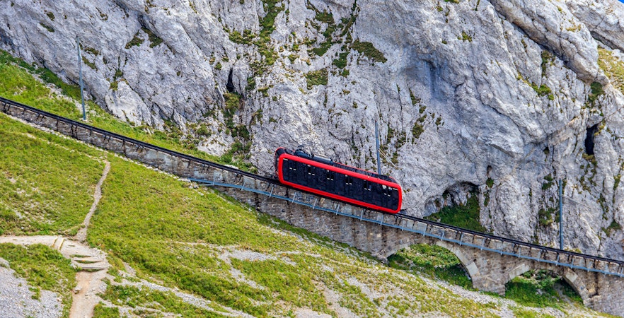 Red train traveling from Lucerne to Mount Titlis with snow-capped mountains in the background.