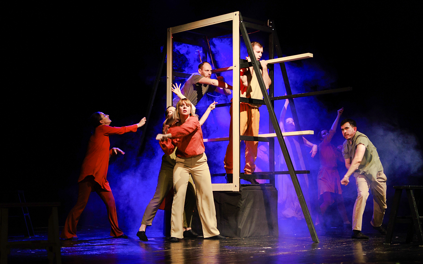 Actors performing a dramatic scene on stage with a wooden structure and blue lighting.