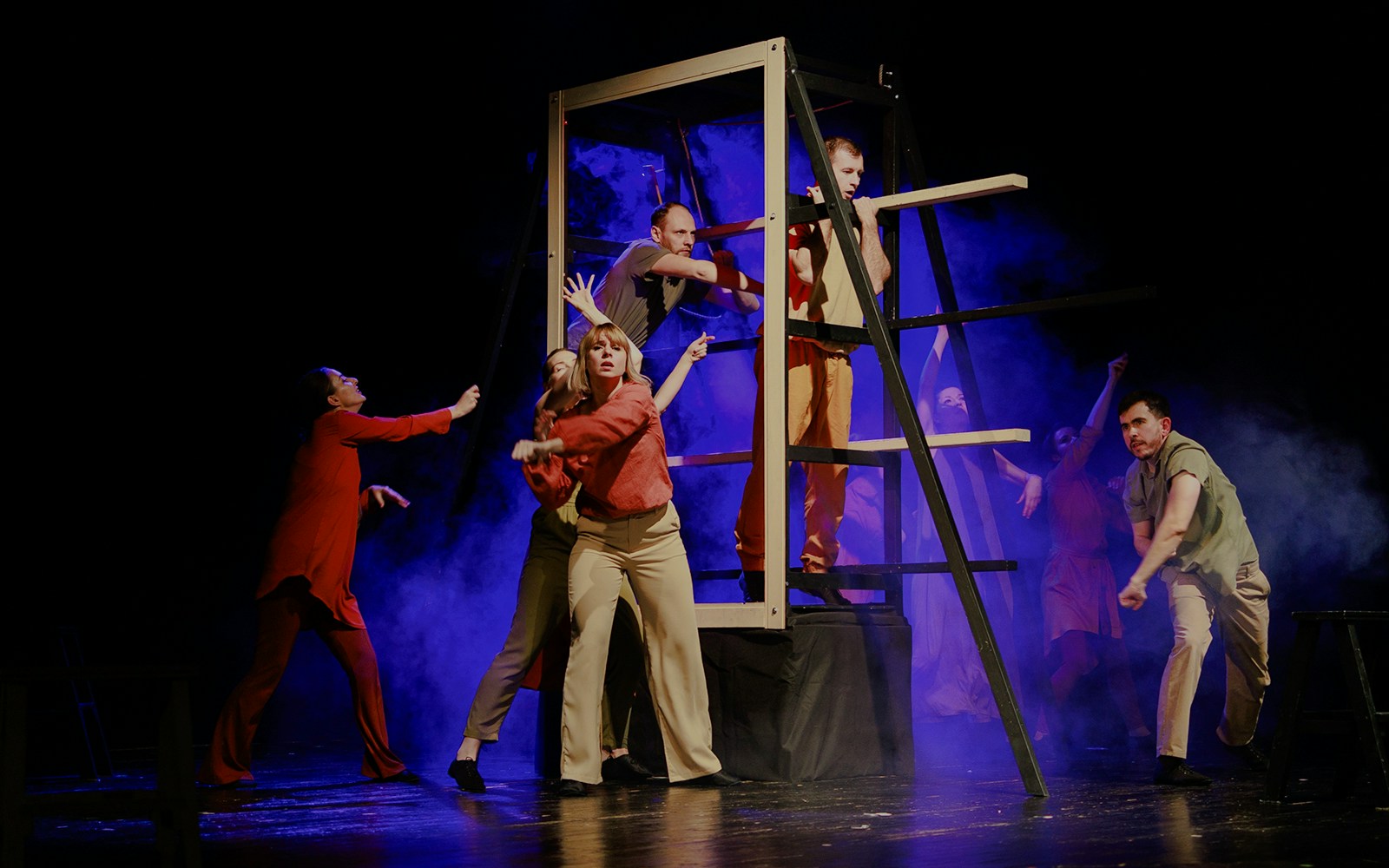 Actors performing a dramatic scene on stage with a wooden structure and blue lighting.