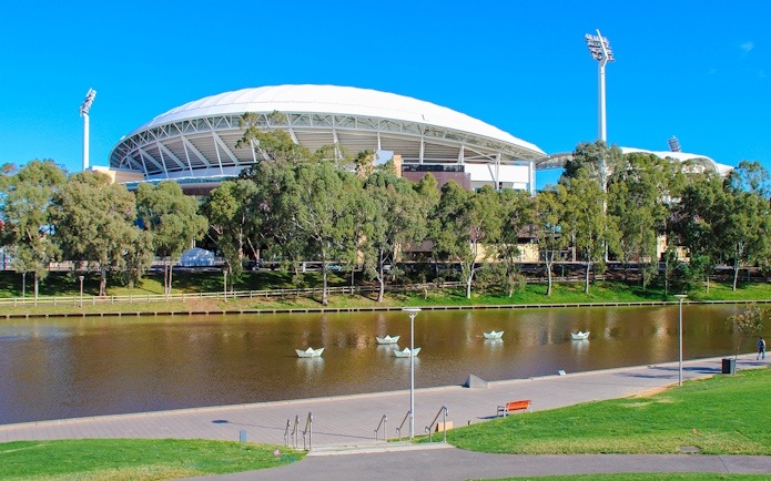 Adelaide Oval Stadium with trees and a lake in the foreground.