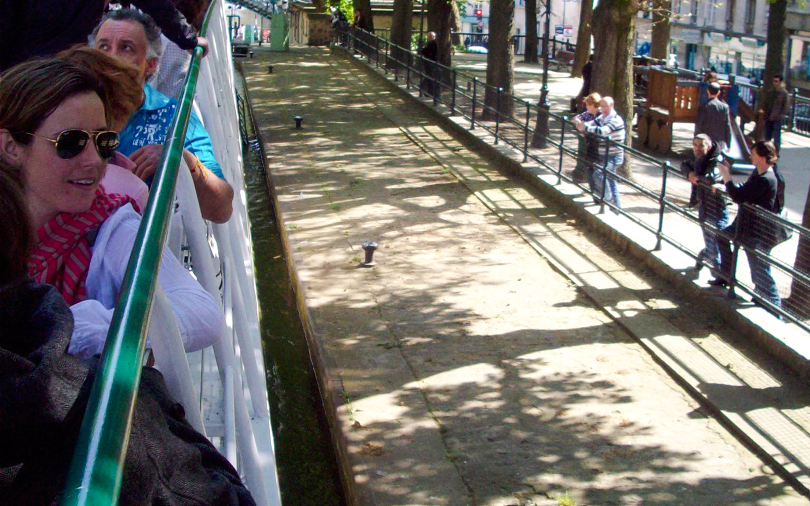 People enjoying a canal cruise in Paris, France, with trees lining the waterway.