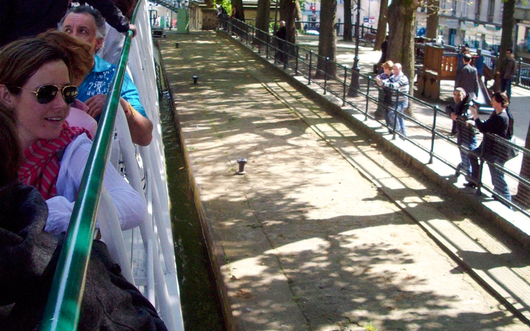 People enjoying a canal cruise in Paris, France, with trees lining the waterway.