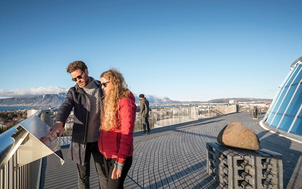 Visitors on Perlan observation deck with Reykjavik skyline and mountains in the background.
