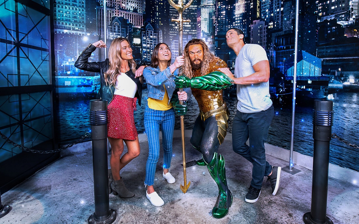 Group posing with superhero statue in city-themed exhibit.