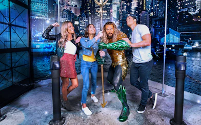 Group posing with superhero statue in city-themed exhibit.