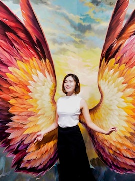 Person posing with colorful angel wings mural at Art in Paradise.