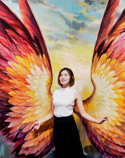 Person posing with colorful angel wings mural at Art in Paradise.