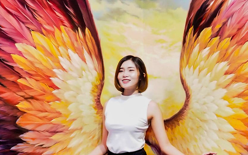 Person posing with colorful angel wings mural at Art in Paradise.