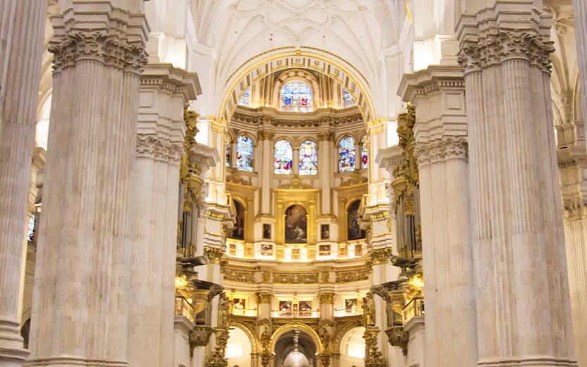 Granada Cathedral interior with ornate columns and stained glass windows.