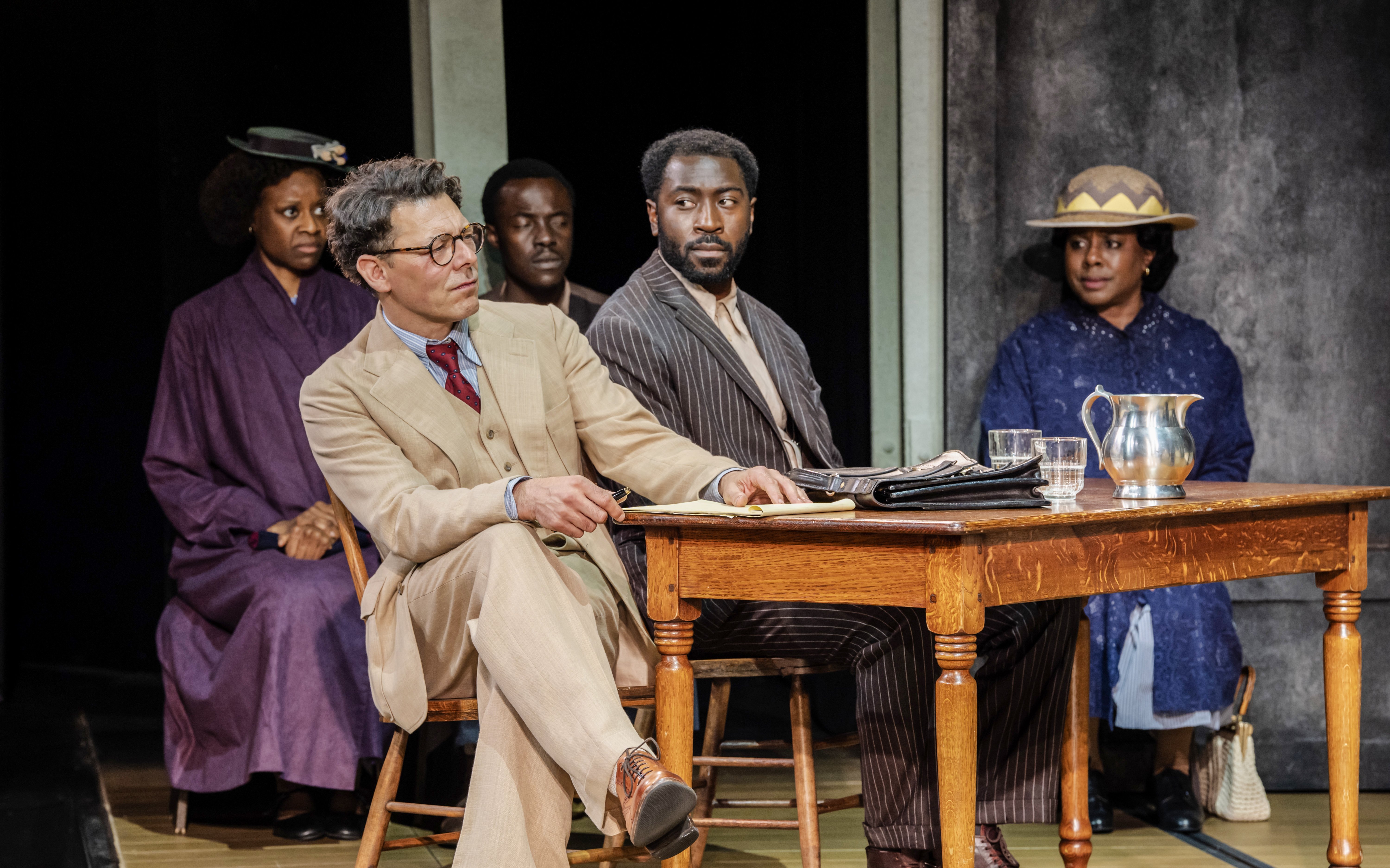 Stage scene from "To Kill a Mockingbird" West End show with actors at a courtroom table.