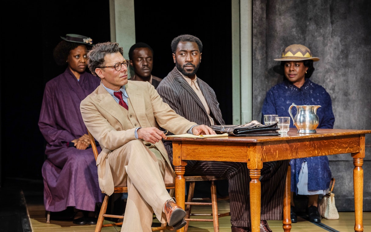 Stage scene from "To Kill a Mockingbird" West End show with actors at a courtroom table.