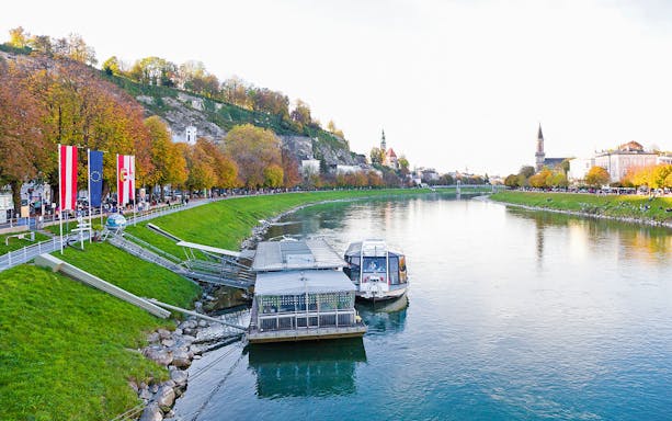 River cruise dock on the Salzach River in Salzburg, Austria, with autumn trees and cityscape.