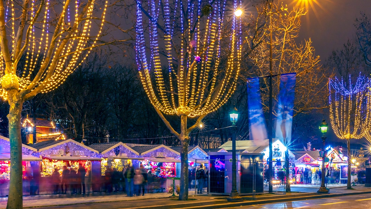 Paris Christmas market with festive lights and decorated stalls at night.