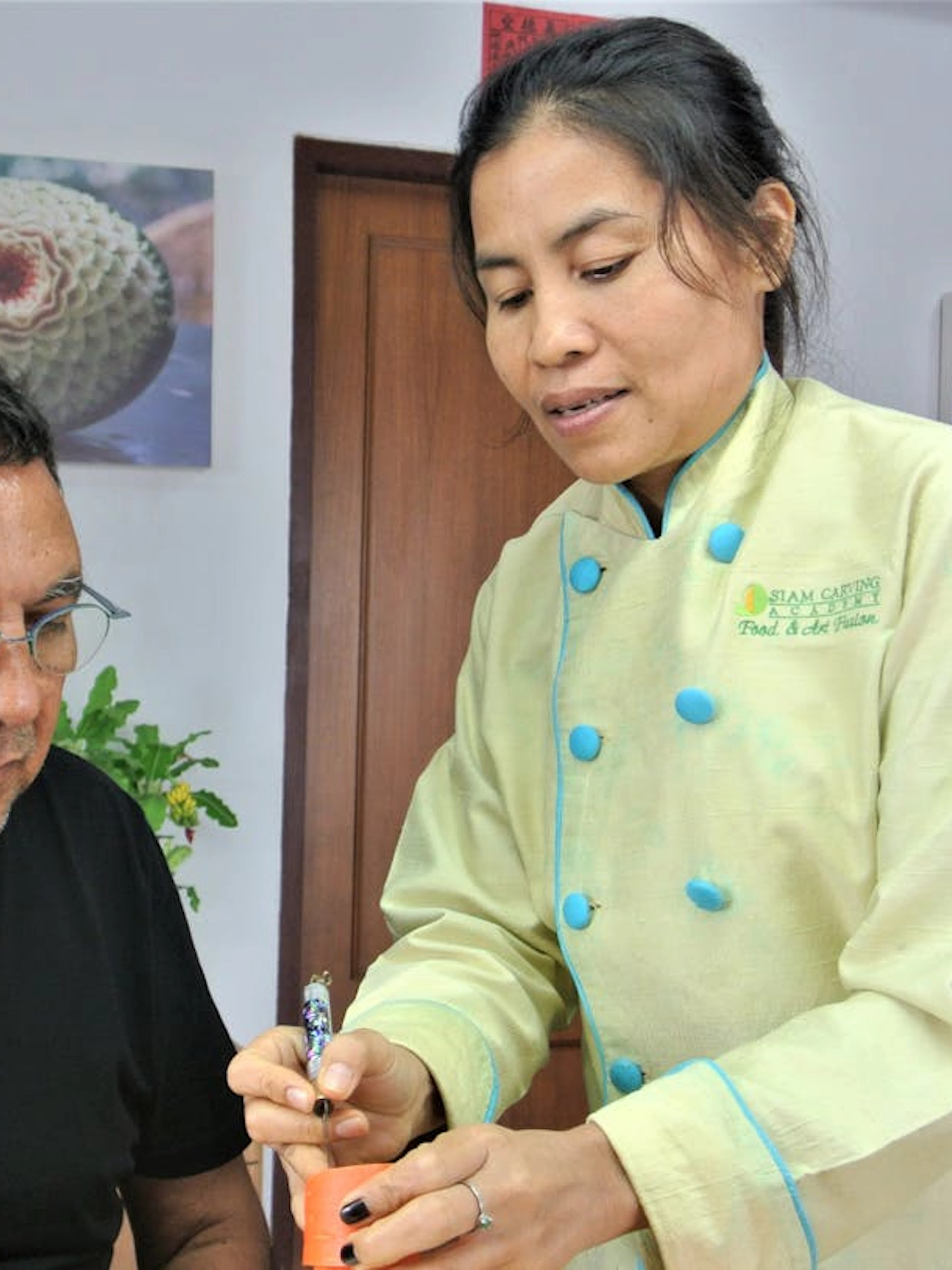 Master carver instructing student in Thai fruit carving at Penthouse Studio.