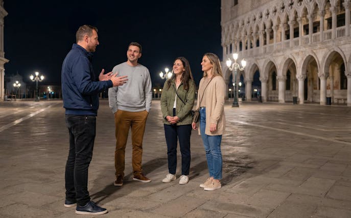 Tour guide with tourists near Doge's Palace in Venice at night.