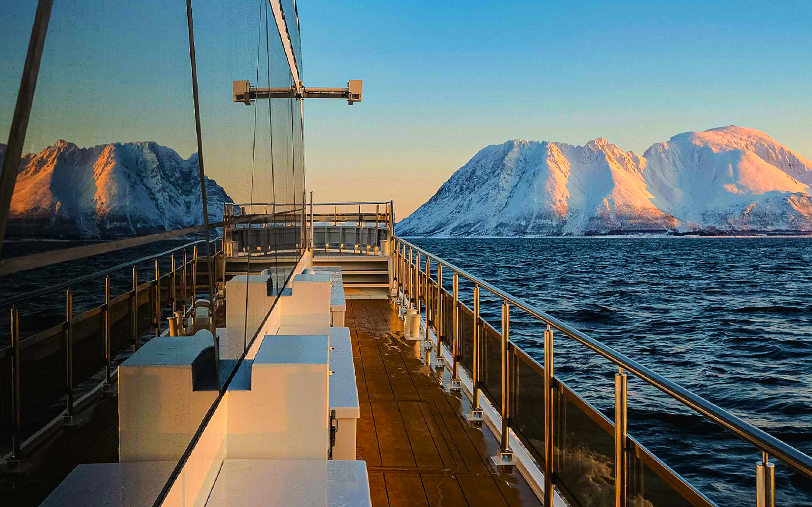 Cruise ship deck with snowy mountains and ocean view at sunset.