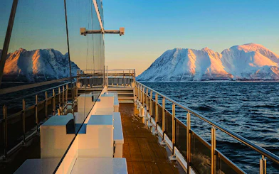 Cruise ship deck with snowy mountains and ocean view at sunset.