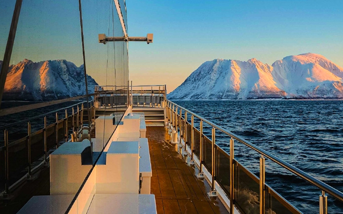 Cruise ship deck with snowy mountains and ocean view at sunset.