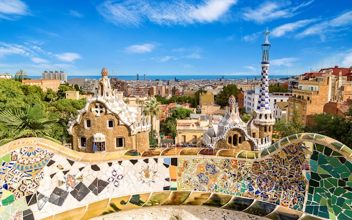 Park Güell's colorful mosaic terrace overlooking Barcelona cityscape.