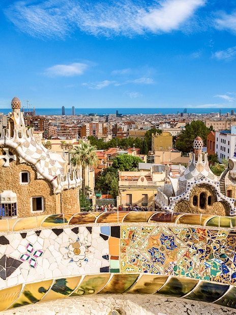 Park Güell's colorful mosaic terrace overlooking Barcelona cityscape.