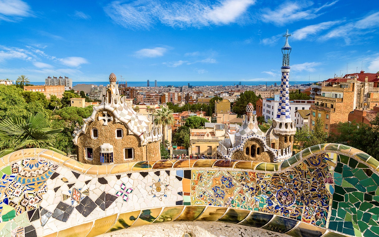 Park Güell's colorful mosaic terrace overlooking Barcelona cityscape.