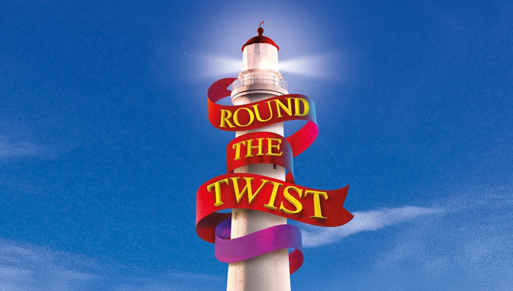 Lighthouse with "Round the Twist" ribbon against blue sky.
