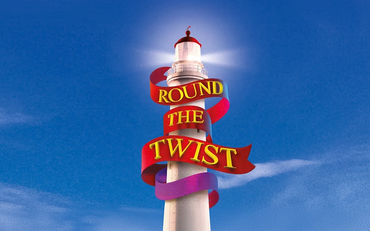 Lighthouse with "Round the Twist" ribbon against blue sky.