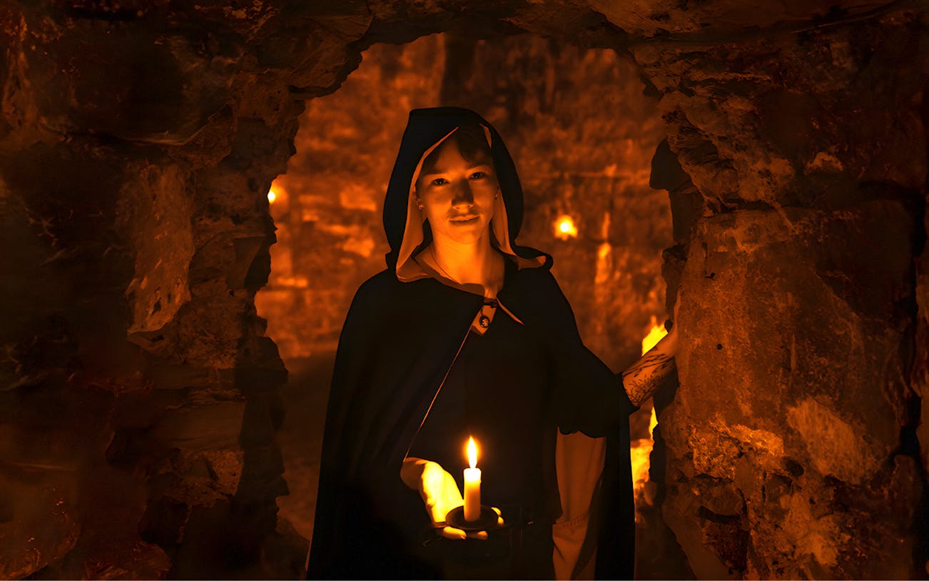 Guide in cloak holding candle in Edinburgh underground vaults on Doomed, Dead and Buried Tour.