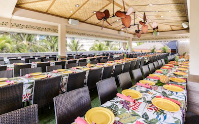 Waikiki Luau Buffet seating area with tropical decor and tables set with yellow plates.