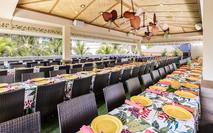 Waikiki Luau Buffet seating area with tropical decor and tables set with yellow plates.