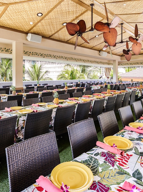 Waikiki Luau Buffet seating area with tropical decor and tables set with yellow plates.