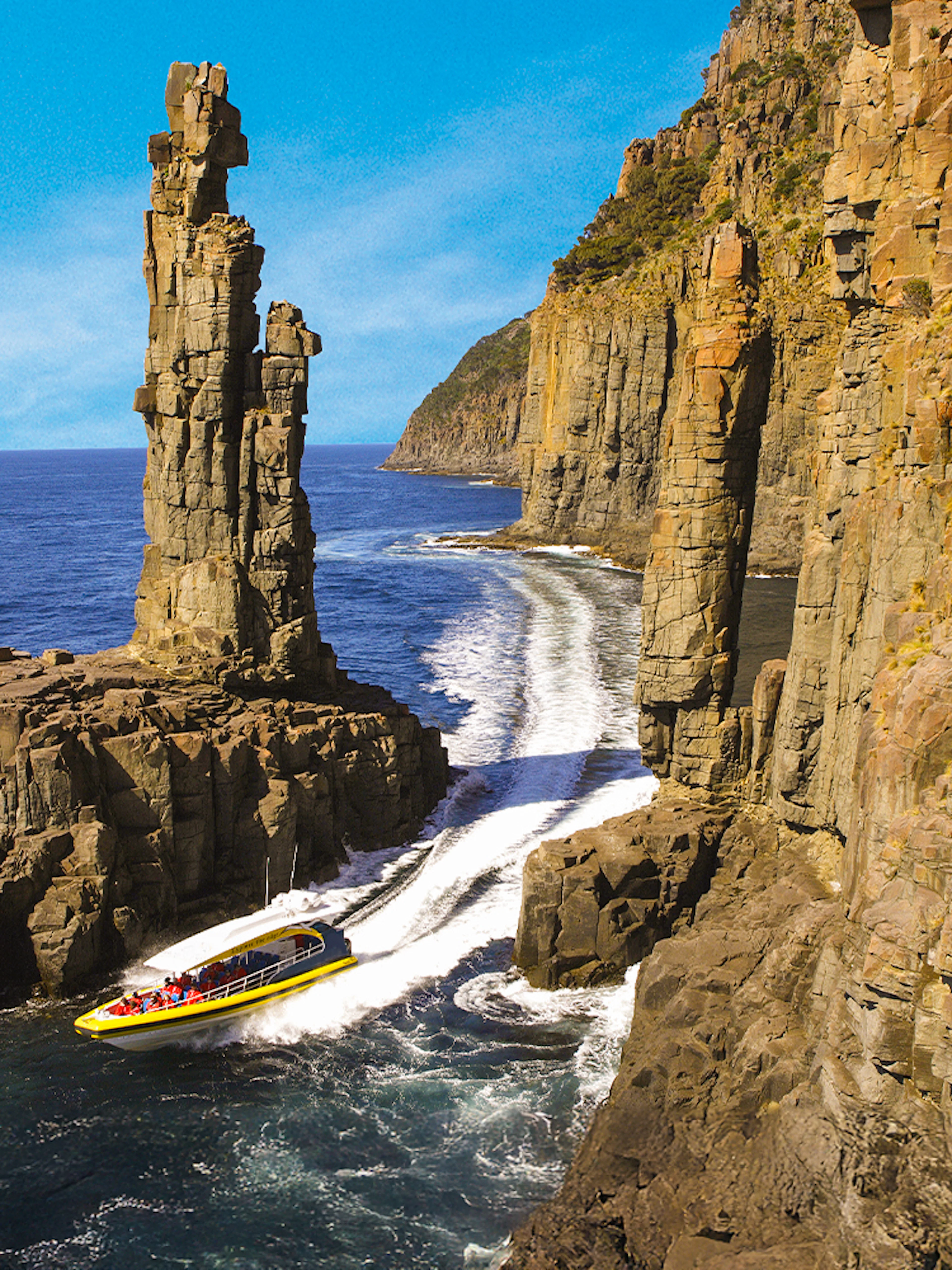 Boat navigating between towering sea cliffs on Bruny Island Wilderness Cruise.