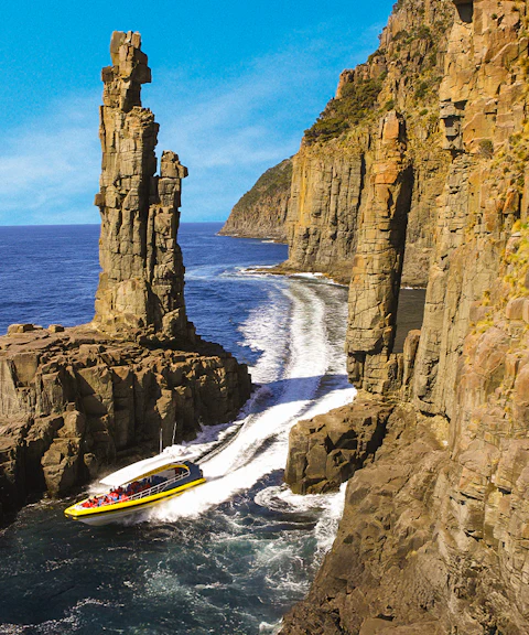 Boat navigating between towering sea cliffs on Bruny Island Wilderness Cruise.