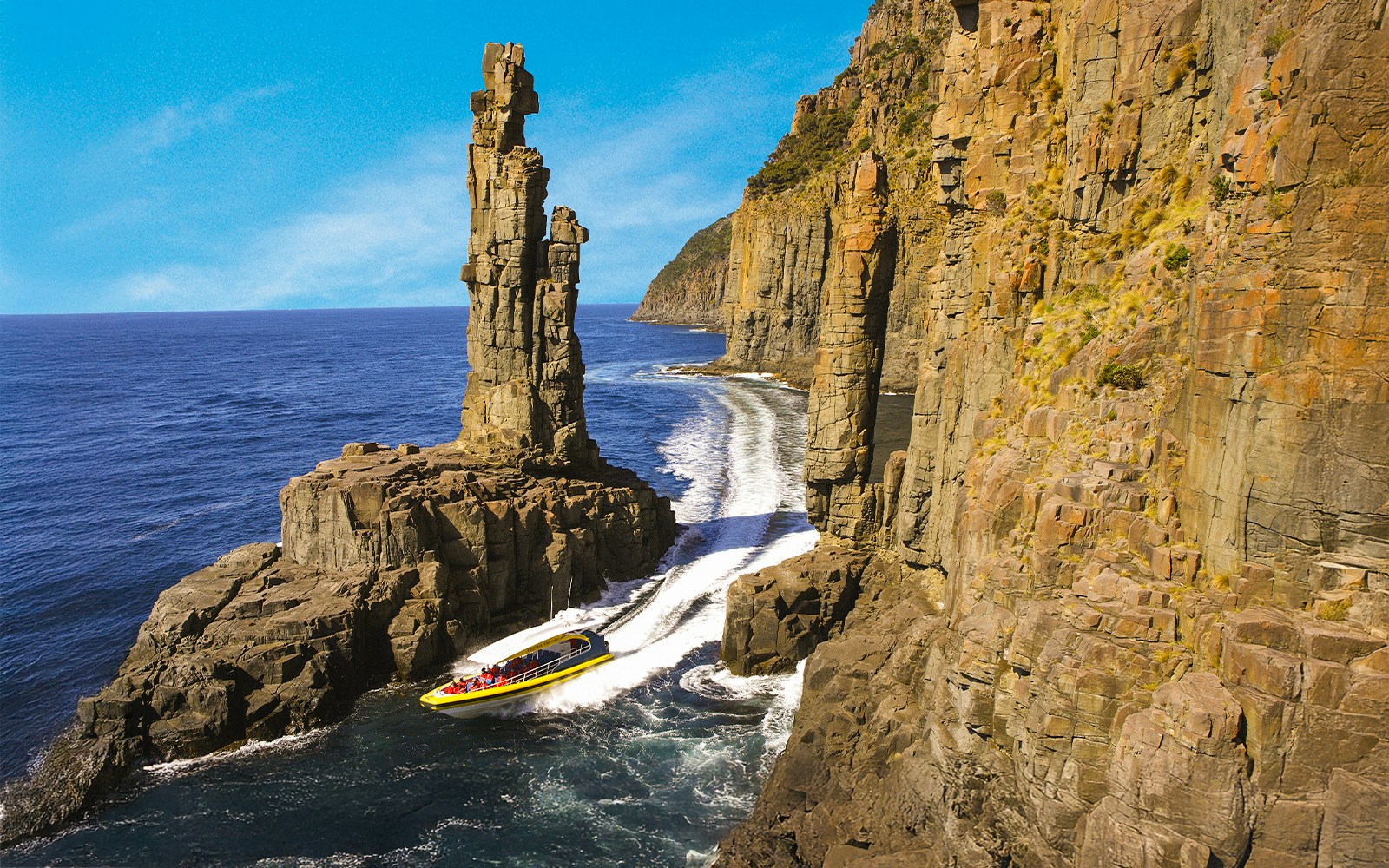 Bruny Island Wilderness Cruise boat navigating rugged coastline with cliffs and sea caves in Tasmania.