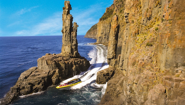 Bruny Island Wilderness Cruise boat navigating rugged coastline with cliffs and sea caves in Tasmania.